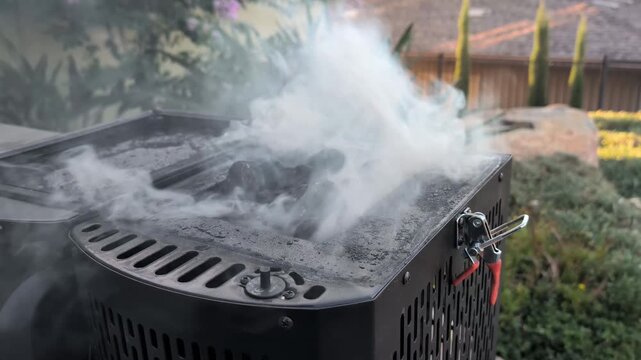 Thick smoke pours from a backyard smoker grill, indicating slow-cooked meat inside. Ideal for culinary blogs or barbecue-themed content.