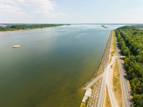Aerial view of the Danube river with a paved cycling path and lush green forests along the banks under a bright sky in Bratislava, Bratislava Region, Slovakia.