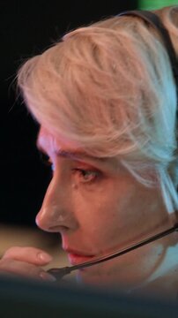 Vertical close up shot of female middle-aged support agent reporting cybersecurity data via headset while monitoring servers in control room