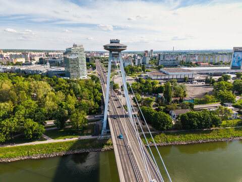 Aerial view of Most SNP bridge with its iconic UFO observation deck spanning the Danube river surrounded by lush green trees and the city skyline Bratislava, Bratislava Region, Slovakia.