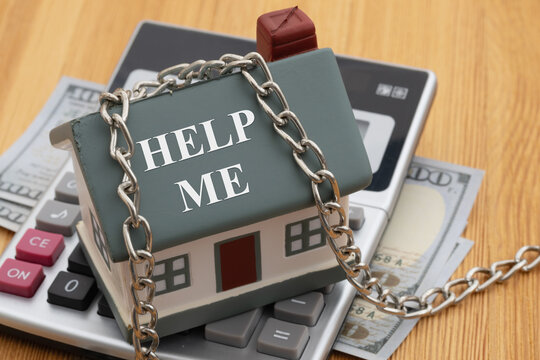 Help Me text on a house with a silver chain on calculator with money on a desk for help with getting a mortgage