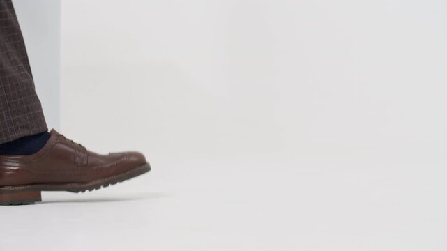 Businessman's legs in leather brogues walking confidently forward on an isolated white background, close-up shot