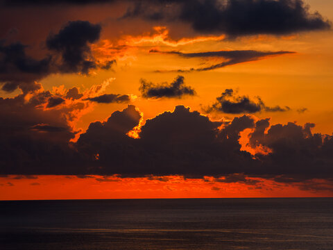 Aerial view of a dramatic sunset over the Indian Ocean at Mauritius Island with dark clouds backlit by vibrant orange and red light Moka District, Mauritius.