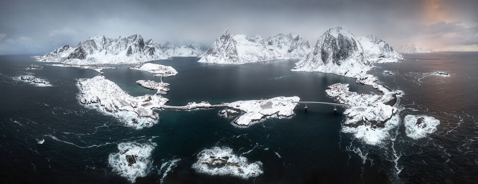Aerial view of the snow-covered Lofoten islands with bridges connecting rocky shores under a dramatic winter sky in Nordland, Norway.