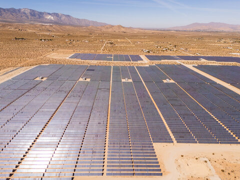 Aerial view of a vast solar farm with rows of photovoltaic panels set against a desert landscape and rugged mountains under a clear sky Lucerne Valley, California, United States.