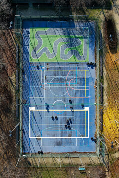 Aerial view of a multi-purpose sports court with a blue surface and a small green circuit track surrounded by trees in Turin, Piedmont, Italy.