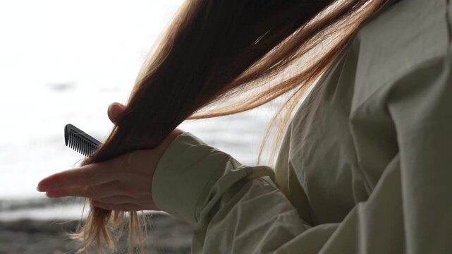 Haircare Combing Outdoors woman combing long hair at the beach against the background of the sea during self care morning routine