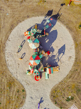 Aerial view of a colorful children's playground with slides and climbing frames on a circular sand pit surrounded by dry grass in Turin, Piedmont, Italy.