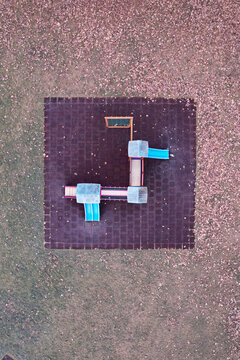 Aerial view of a colorful playground structure with blue slides on a dark square mat surrounded by autumn leaves in Turin, Piedmont, Italy.