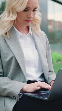 Attractive stylish caucasian business woman working on a laptop sitting on street city building background. Modern lifestyles of business lady. Slow motion.