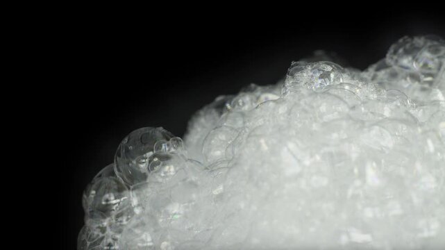 Close-Up of White Soap Foam Bubbles Popping on Black Background.
A high-detail macro shot featuring a cluster of white soap suds and iridescent bubbles against a dark background.