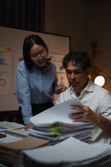 Naklejka premium Two business people collaborating on a project, analyzing data and reviewing documents late at night, working overtime in an office toward a deadline