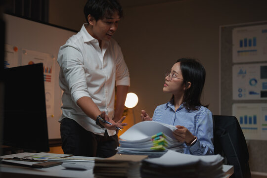 Business colleagues discussing project deadlines and managing workload during late night overtime, collaborating on tasks in a dimly lit office environment