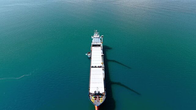 Flyover the long empty cargo ship equipped with two large heavy-lift cranes. Bulk carrier on the turquoise waterscape.