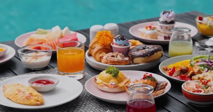 Assorted breakfast spread including eggs benedict, omelet, fresh tropical fruits, pastries on wooden table by turquoise swimming pool, resort vacation dining, food travel photography