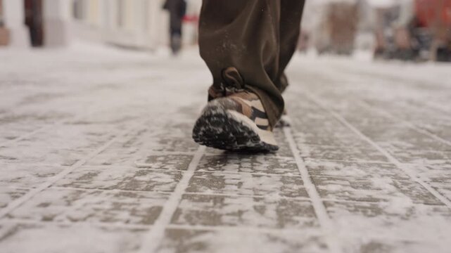 Brisk snowy street closeup steps crossing central avenue, patterned tiles dusted with snow, durable walking shoes, purposeful pace, bundled pedestrians in background, dynamic urban energy, lowangle