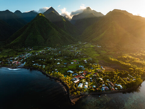 Aerial view of lush green volcanic mountains and a coastal village during golden hour Moorea-Maiao, Windward Islands, French Polynesia.