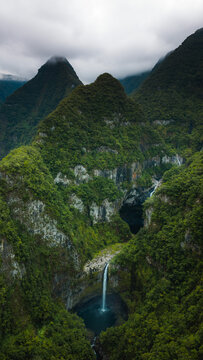 Aerial view of the massive waterfalls cascading down lush green volcanic cliffs in the heart of the tropical forest in La Reunion, France.