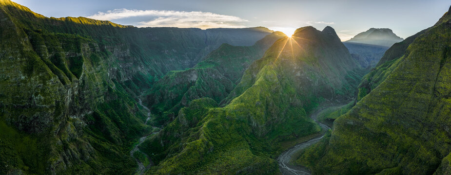 Aerial view of the lush volcanic valley with steep green ridges and a winding river during a golden sunrise La Reunion, France.