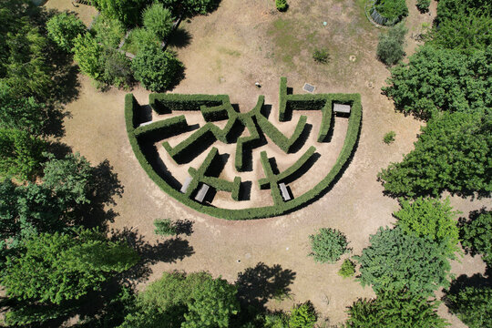 Aerial view of a semicircular hedge maze surrounded by green trees and dry grass in Turin, Piedmont, Italy.