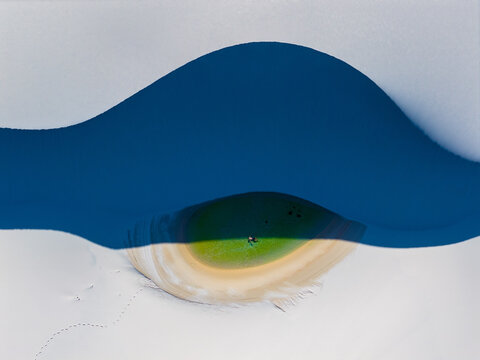 Aerial view of the Parque Nacional dos Lencois Maranhenses with a vibrant green lagoon nestled between white sand dunes and a person swimming in Lencois Maranhenses, MA, Brazil.