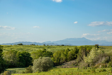 Obraz premium Picturesque rural landscape with green valley and trees against distant majestic taurus mountains under clear blue sky. Beautiful sunny spring day. Ilica, Antalya, Turkey.