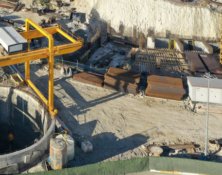 Aerial view of a busy construction site featuring a large yellow gantry crane, a deep circular excavation shaft, and stacks of rebar in Avcilar, Istanbul, Turkiye.