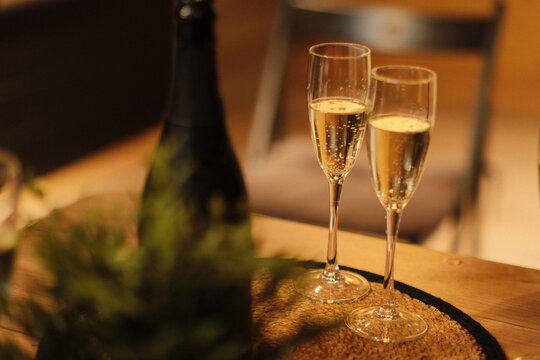 Two glasses of champagne and a bottle on a table in warm golden light. Luxury romantic dinner or celebration evening scene, closeup