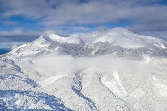 Aerial view of the snow-covered peaks and frosted forests with a thick layer of clouds in the valley of Cerreto Laghi, Emilia-Romagna, Italy.