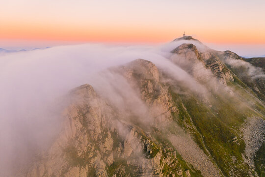 Aerial view of a mountain peak with a communication tower partially shrouded in thick clouds under a pink sunset sky Cerreto Laghi, Emilia-Romagna, Italy.