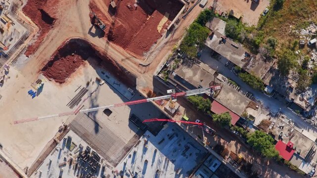 Top-down aerial perspective showing a large construction site with cranes rotating and machinery moving, highlighting the initial phases of building a new modern architectural structure
