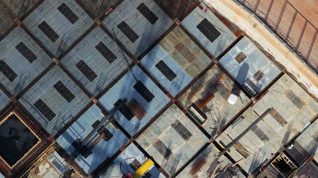 Top-down aerial view capturing the various stages of building construction, showcasing the architectural grid, foundation work, concrete pouring, and progression from the ground floor up