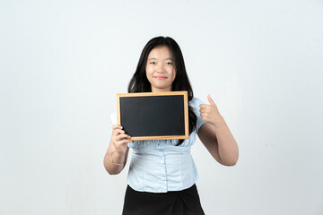 Fototapeta premium Happy Asian girl holding small blackboard and showing thumbs up sign on white background