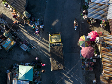 Aerial view of a yellow truck driving through a busy street market with colorful umbrellas and people Kemalang, Central Java, Indonesia.