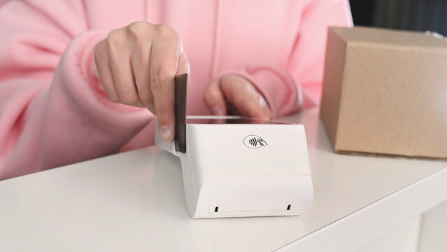 Paying with a magnetic stripe card for parcel delivery. Electronic cashless payments. Online shopping. A woman enters a PIN code on a wireless payment terminal.