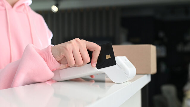 Paying with a magnetic stripe card for parcel delivery. Electronic cashless payments. Online shopping. A woman enters a PIN code on a wireless payment terminal.