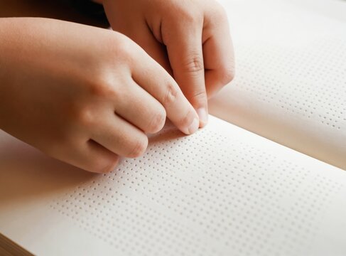 Child reads braille text using fingertips. Person learns braille alphabet in book. Tactile reading promotes learning and independence. Accessible education for visually impaired.