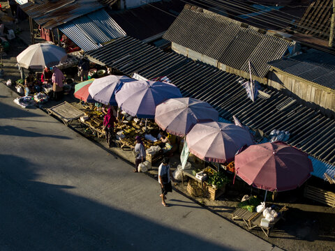 Aerial view of traditional market stalls with colorful umbrellas and people walking along the street in Kemalang, Central Java, Indonesia.