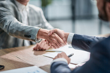 Two professionals shake hands over a wooden table © ASDF