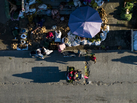 Aerial view of a street market with vendors, produce sacks, a blue umbrella, and people on motorcycles in Kemalang, Central Java, Indonesia.