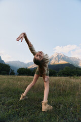Fototapeta premium Woman dancer outdoors in a grassy field with distant mountains, expressing joy and freedom, mid motion, casual outfit, lifestyle portrait under bright sky