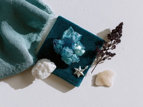 Overhead flat lay of blue crystal cluster, silver star pendant, white rock, dried flower, and teal fabric on pure white background for mood board design