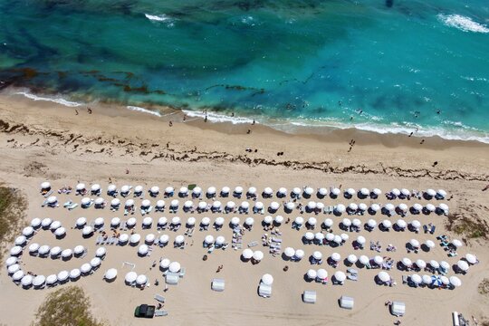 Aerial view of Singer Island beach featuring rows of white umbrellas along the sandy shore and turquoise ocean water in Riviera Beach, Florida, United States.