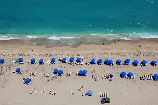 Aerial view of Singer Island beach with rows of blue umbrellas and people relaxing by the turquoise ocean waves Riviera Beach, Florida, United States.
