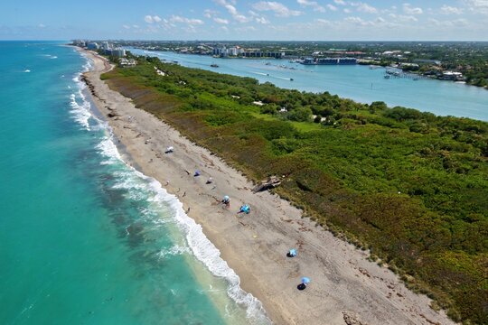 Aerial view of the turquoise coastline and sandy beach with umbrellas bordering lush green vegetation and the Jupiter Inlet Jupiter, Florida, United States.