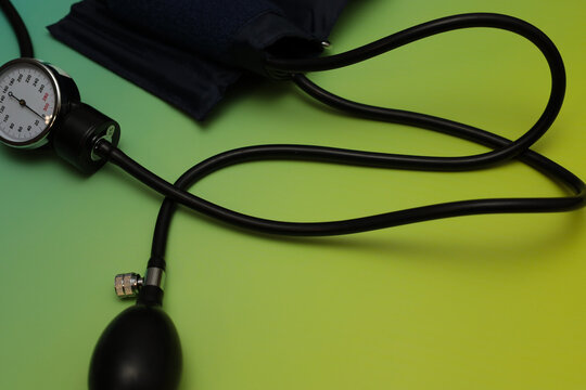 ​A manual sphygmomanometer with a cuff, bulb, and analog pressure gauge rests on a vibrant green and yellow gradient background.