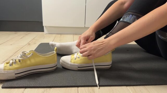 White Woman Tying Yellow Sneakers On Mat, Lacing Sturdy Canvas Shoes With Focused Fingers, Energetic Prerun
