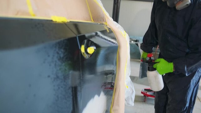 Professional auto body technician spraying degreaser on repaired vehicle panel before automotive painting and refinishing process in collision repair workshop.