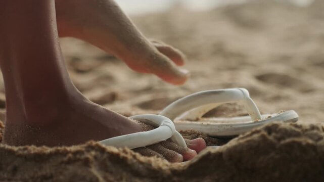 Bare foot lifting from sandy sandal, quick closeup of toes releasing white strap, grains scattering as foot rises, playful motion and energetic rhythm, child or teen skipping along shoreline, warm