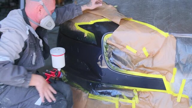 Professional auto painter applying glossy clear coat with spray gun after aerosol blending solvent treatment during automotive bumper refinishing process. applying clear coat with spray gun